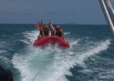Grupo de pessoas acenando durante passeio de banana boat oferecido pela FNS Turismo Náutico, que também faz passeios de lancha panorâmicos, translados e charter de lancha