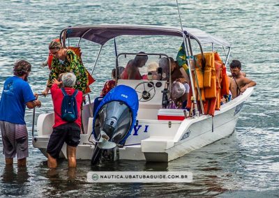 Pessoas sentadas e uma mulher desembarcando com auxílio da equipe da Lucky Turismo, que oferece a opção de alugar a lancha para realizar passeios pelas praias e ilhas de Ubatuba