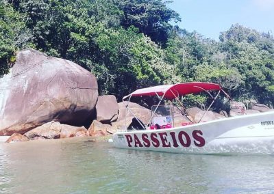 Em dia ensolarado e com grande formação rochosa ao fundo, que se assemelha a uma baleia, a lancha descansa em águas calmas durante passeio panorâmico cujo principal diferencial é o conhecimento empírico do Fábio, caiçara nativo da Fortaleza