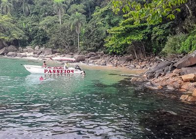 Lancha ancorada sob águas cristalinas com densa vegetação nativa ao fundo e uma praia de Ubatuba excelente para mergulho