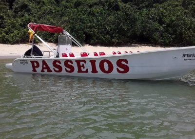 Mulher sentada na faixa de areia da Praia do Costa bem próxima da embarcação, ancorada e em destaque no primeiro plano da imagem