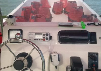 Assentos com coletes salva vidas no plano de fundo e cabine de comando da lancha em destaque no primeiro plano