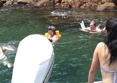 Garota jovem observa família aproveitando, com flutuadores e máscaras, equipamentos e acessórios incluídos nos passeios de lancha da Sol e Sal