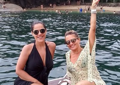 Praia do Português ao fundo com duas jovens mulheres sorrindo para a foto durante o final do roteiro de um dos inúmeros passeios de lancha oferecidos pela Sol e Sal