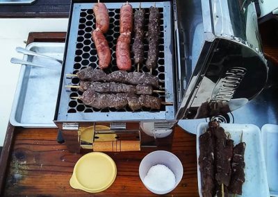 Espetos de linguiça e carne em churrasqueira, disponível gratuitamente durante o aluguel de lanchas no Itaguá, em Ubatuba
