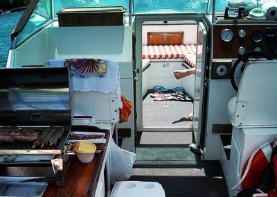 A bordo da lancha, churrasco sendo preparado enquanto pessoa relaxa na proa
